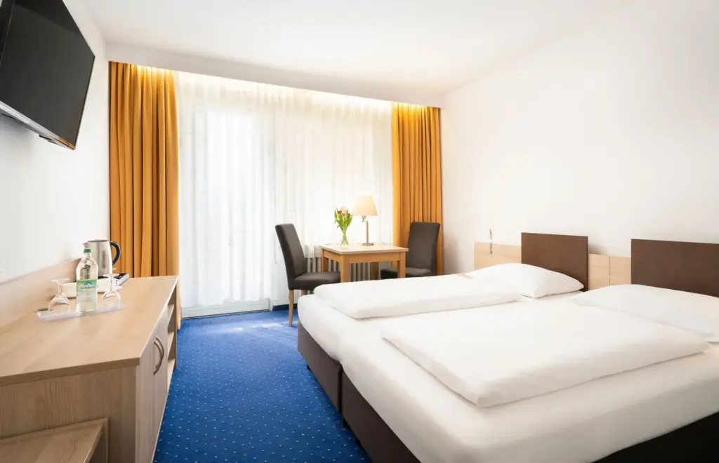 Hotelzimmer mit Doppelbett, goldenem Vorhang und blauem Teppich